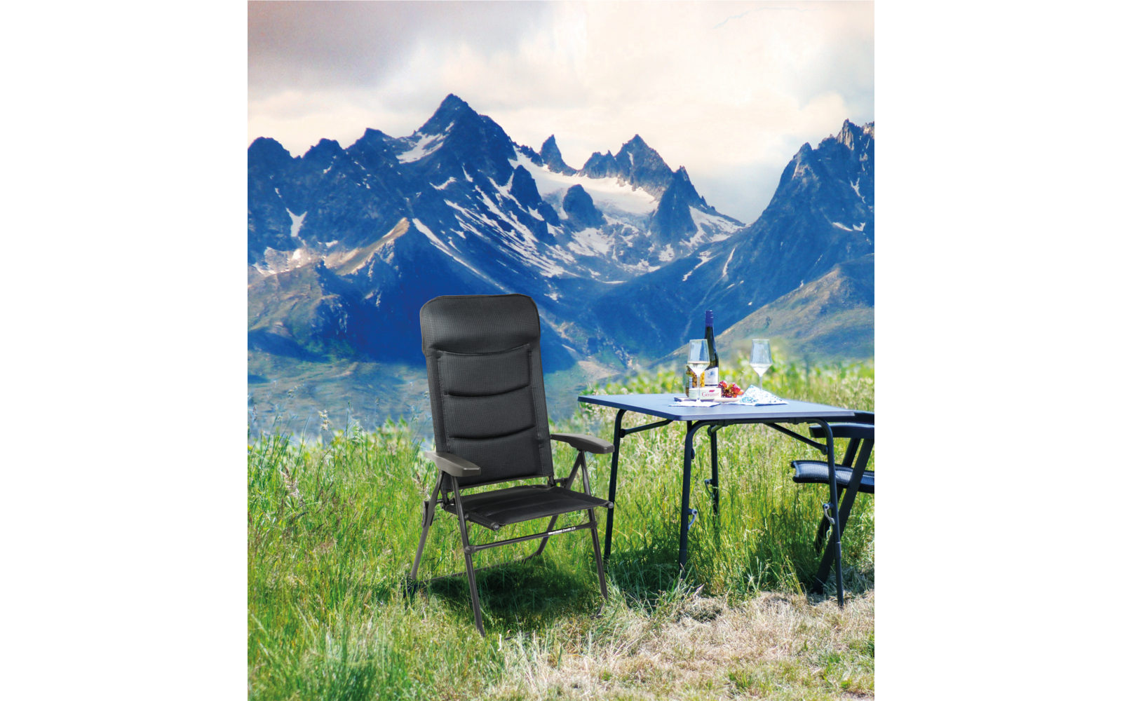 Berglandschaft mit schneebedeckten Gipfeln, Wiese im Vordergrund, ein Klappstuhl und ein Tisch mit einer Wasserflasche und einem Glas