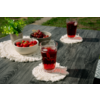 Mesa de madera oscura con dos vasos de bebida roja con hielo sobre posavasos blancos, dos cuencos con fresas y cerezas y una pequeña planta verde en maceta; césped al fondo