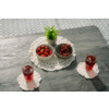 Mesa de madera gris con un tapete blanco de ganchillo, dos cuencos pequeños grises con fresas y uvas rojas, una pequeña planta en maceta verde y dos vasos con líquido rojo sobre posavasos blancos
