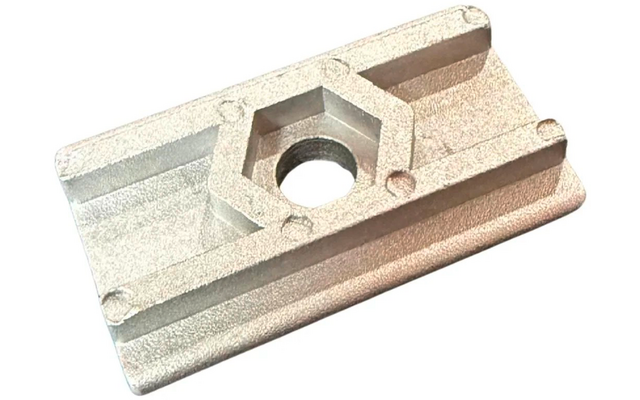 Pièce métallique rectangulaire argentée à surface mate, bossage hexagonal central avec trou rond traversant, deux nervures longitudinales parallèles et quatre petites empreintes rondes aux angles