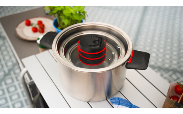 Une casserole avec de l'eau bouillante sur une cuisinière, avec un insert passoire contenant des pâtes rouges au-dessus