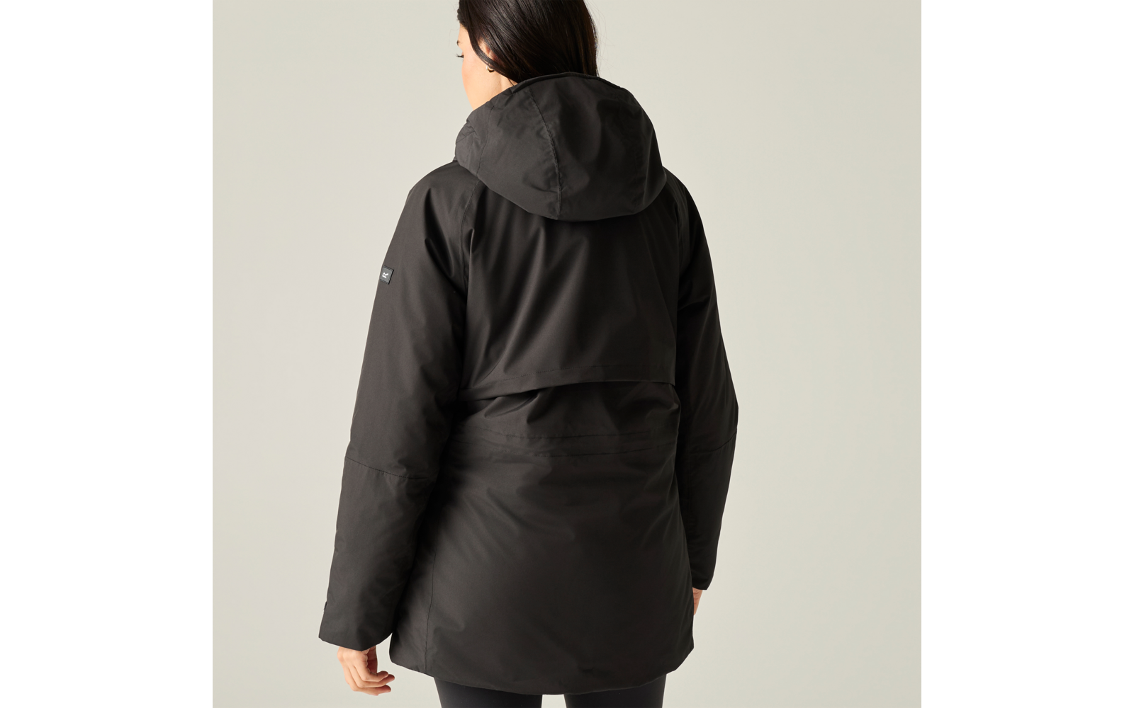 Person seen from the back wearing a black hooded jacket against a light background