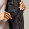 Two hands holding a black drawcord with a cord lock inside a black jacket; visible zipper placket and beige garment underneath