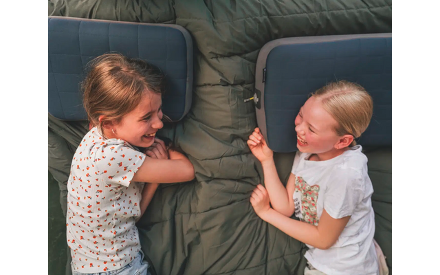 Due ragazze sorridenti sdraiate con la testa su un cuscino su una coperta verde