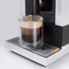 Kaffeemaschine füllt ein doppelwandiges Glas mit dunkelbraunem Kaffee und sichtbarer Crema auf einer Metallabtropfschale