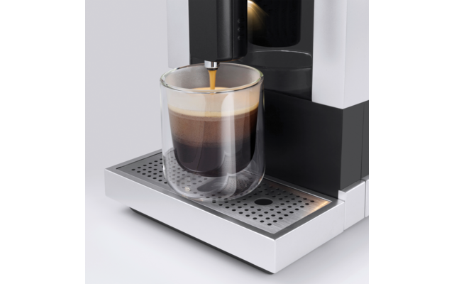Kaffeemaschine füllt ein doppelwandiges Glas mit dunkelbraunem Kaffee und sichtbarer Crema auf einer Metallabtropfschale