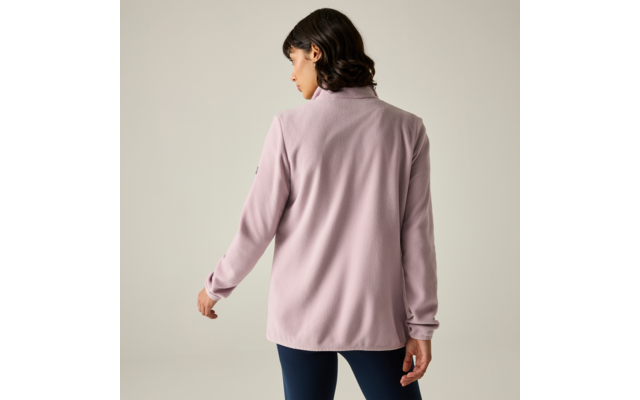 Persona vista da dietro con capelli corti e scuri, indossa una giacca rosa chiaro e pantaloni scuri aderenti su sfondo chiaro neutro