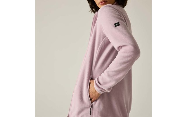 Vista laterale di una persona che indossa una giacca in pile rosa chiaro, mano nella tasca con zip, mento e bocca visibili, piccolo marchio nero sulla manica, sfondo chiaro