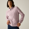 Persona con giacca in pile rosa chiaro con cerniera e pantaloni scuri, in piedi davanti a uno sfondo chiaro uniforme, mani sui fianchi