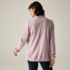 Persona vista da dietro con capelli corti e scuri, indossa una giacca rosa chiaro e pantaloni scuri aderenti su sfondo chiaro neutro