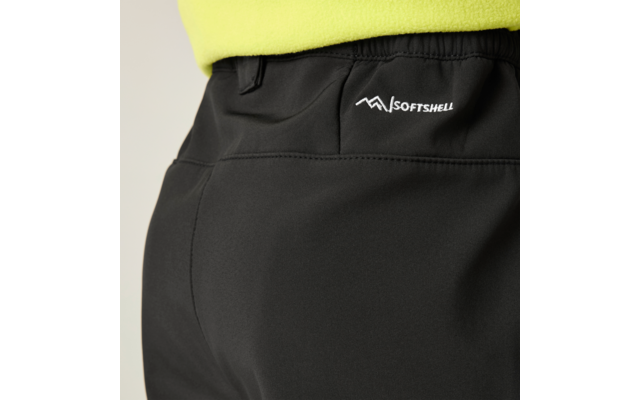Nahaufnahme der Rückseite einer schwarzen Softshell-Hose mit elastischem Bund, sichtbarer Naht und weißem SOFTSHELL-Logo rechts; unterer Saum eines gelbgrünen Oberteils