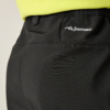 Nahaufnahme der Rückseite einer schwarzen Softshell-Hose mit elastischem Bund, sichtbarer Naht und weißem SOFTSHELL-Logo rechts; unterer Saum eines gelbgrünen Oberteils