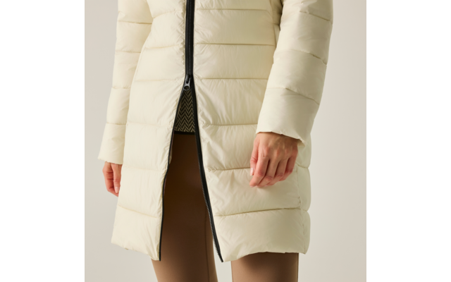 Vista parziale di una persona dalle anche con un cappotto imbottito color avorio e cerniera centrale parzialmente aperta, sotto una maglia con motivo e leggings marroni, mani visibili ai lati, sfondo neutro