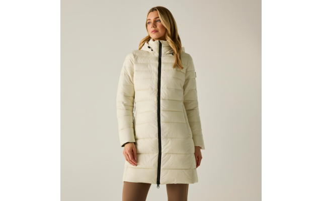 Donna su sfondo chiaro che indossa un cappotto trapuntato beige chiaro con cappuccio e zip nera, lunghezza al ginocchio, pantaloni beige visibili