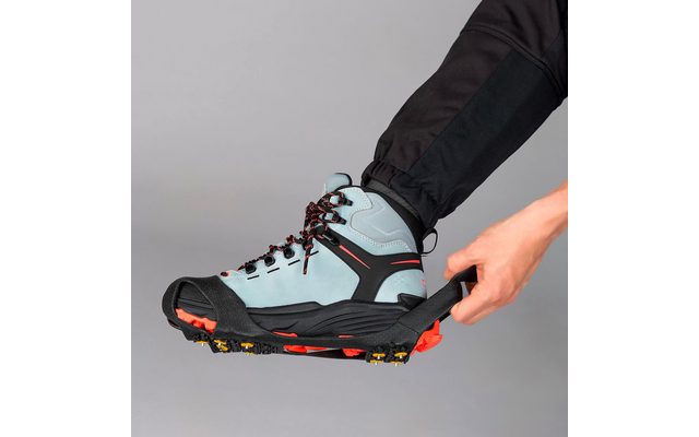 Hand zieht eine schwarze Gummitraktionssohle über die Spitze eines hellblauen Wanderschuhs; schwarzes Hosenbein und grauer Hintergrund