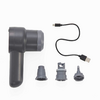 Dunkelgraues Handgerät mit zylindrischem Kopf und Griff auf weißem Hintergrund, daneben USB-Ladekabel und drei austauschbare Aufsätze