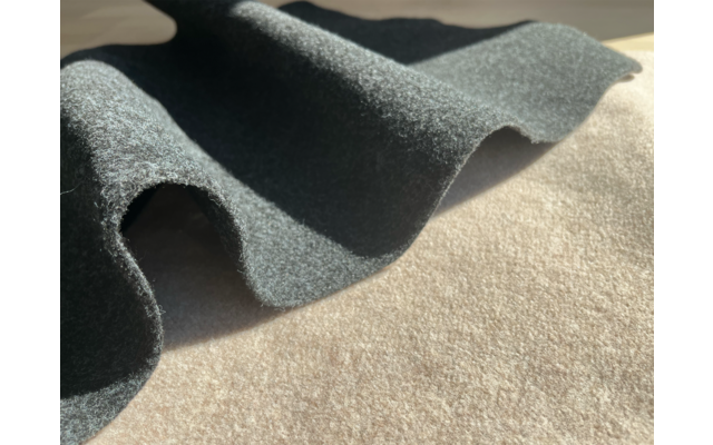 Grauer, strukturierter Stoff in welligen Falten auf beigem Untergrund, Sonnenlicht wirft Schatten und helle Stellen