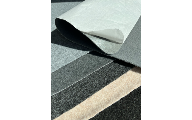 Mehrere überlappende Filz- oder Stoffbahnen in Grau-, Schwarz- und Beigetönen; eine weiße Schicht ist an einer Ecke nach oben gebogen