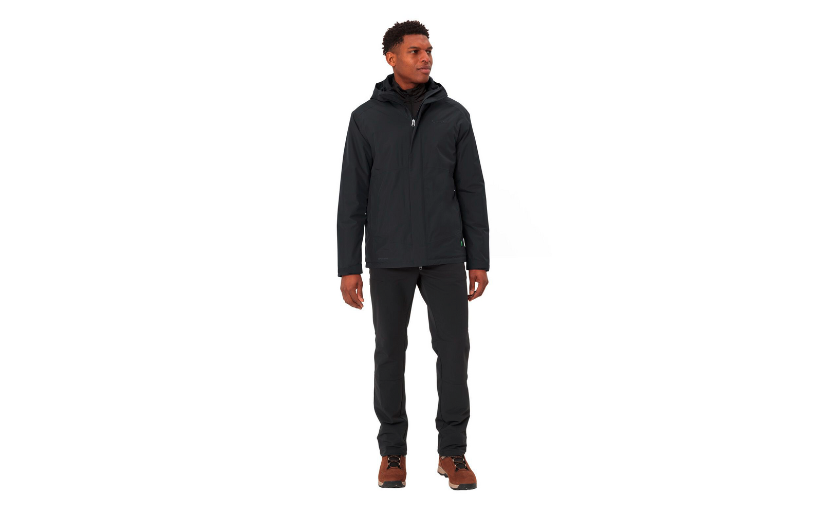 Een man draagt een zwarte jas en zwarte broek met bruine schoenen, staand voor een witte achtergrond