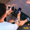 Een man met tatoeages houdt twee smartphones vast met een app in beeld, zittend op de vloer