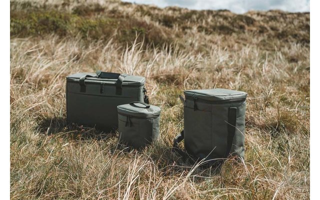 Tres neveras verde oliva de diferentes tamaños sobre hierba seca, dunas de arena al fondo