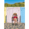 Persona sentada en una silla plegable frente a casetas de playa coloridas, con arena y dunas al fondo