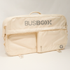 Sac beige souple avec poignée, deux poches avant zippées et inscription grise "BUSBOXX" sur fond neutre