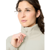 Close-up of a person with hair pulled back, holding the zipper pull of a light-colored fleece jacket at the chin, white background