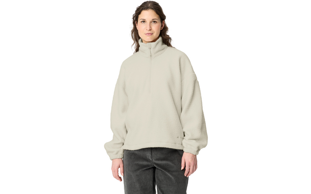 Person standing facing the camera against a white background, wearing a light beige fleece pullover with stand collar and quarter zipper, long sleeves, relaxed fit, dark trousers, hands visible at sides