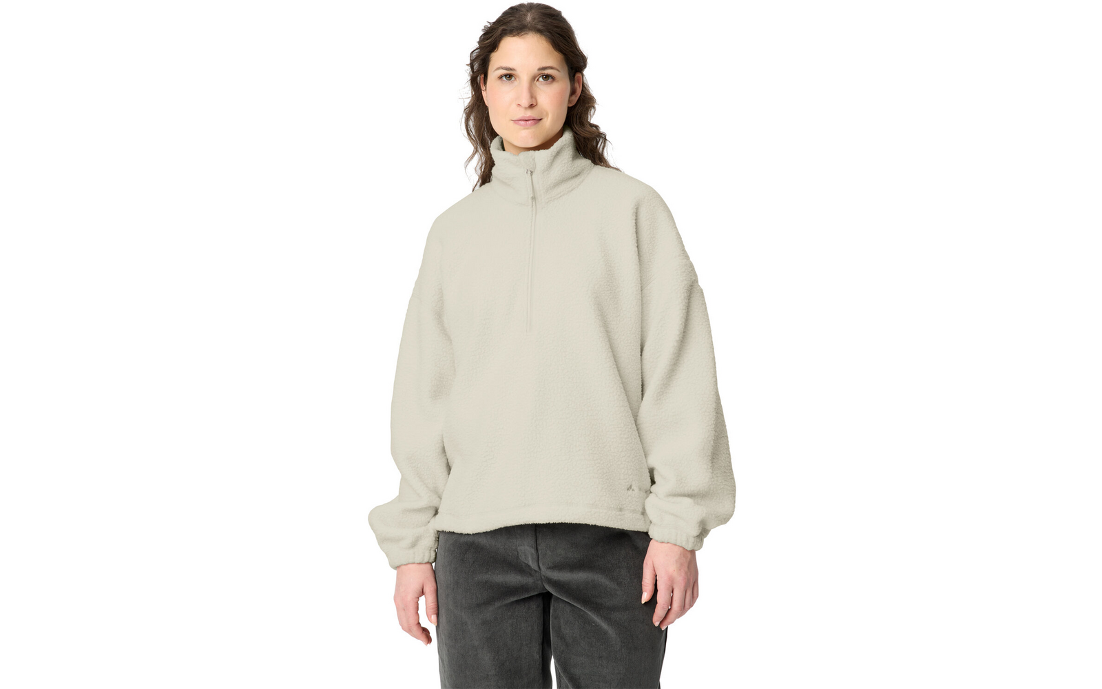 Person standing facing the camera against a white background, wearing a light beige fleece pullover with stand collar and quarter zipper, long sleeves, relaxed fit, dark trousers, hands visible at sides