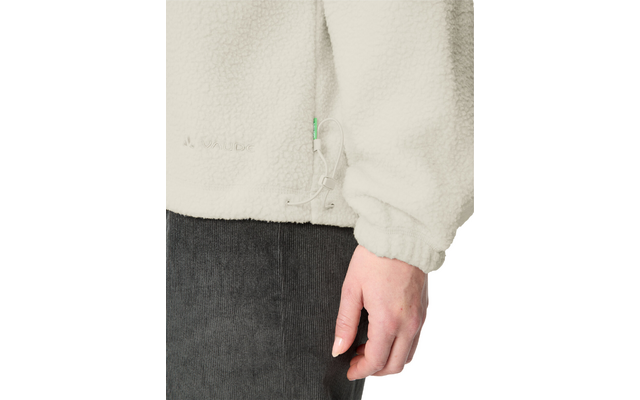 Hand of a person beside a cream fleece jacket with drawcord and zipper; dark gray corduroy pants visible below