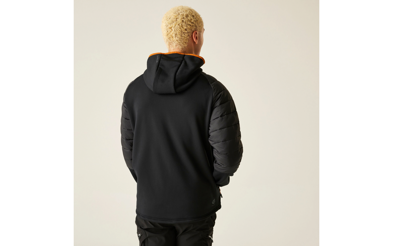 Person von hinten, trägt schwarzen Hoodie und dunkle Hose, steht vor hellem Hintergrund