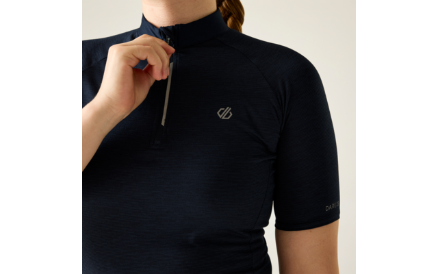 Oberkörper einer Person in dunkelblauem kurzärmeligen Oberteil mit kurzem Reißverschluss vorn, Hand hält den Reißverschluss, kleines Logo auf der Brust, Kinn und Nacken sichtbar, Haare zu einem Zopf gebunden, heller Hintergrund