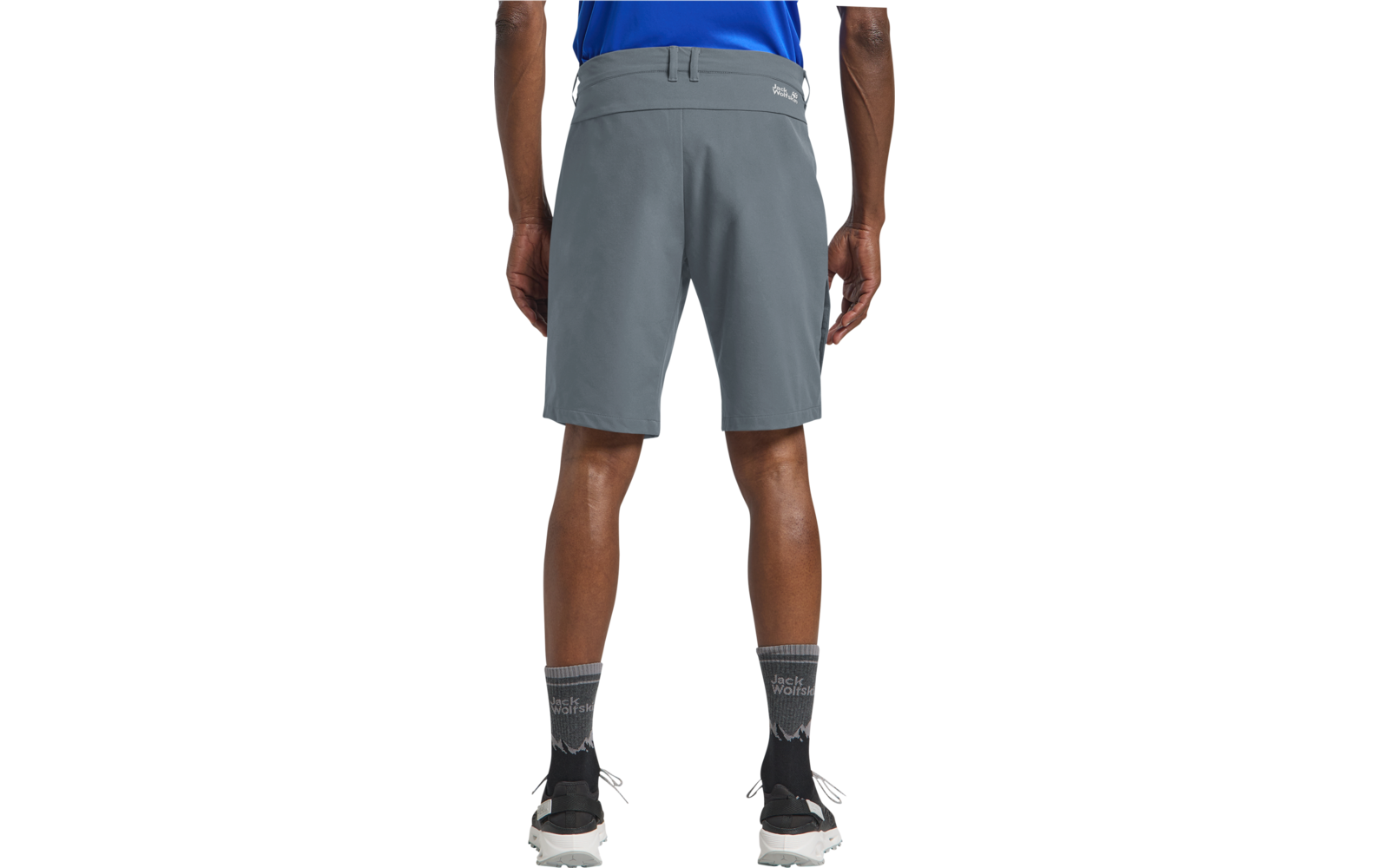 Achteraanzicht van een persoon van taille tot kuit, grijze knielange korte broek, blauwe shirtzoom, grijze sokken met patroon, zwarte sportschoenen met witte zolen, witte achtergrond