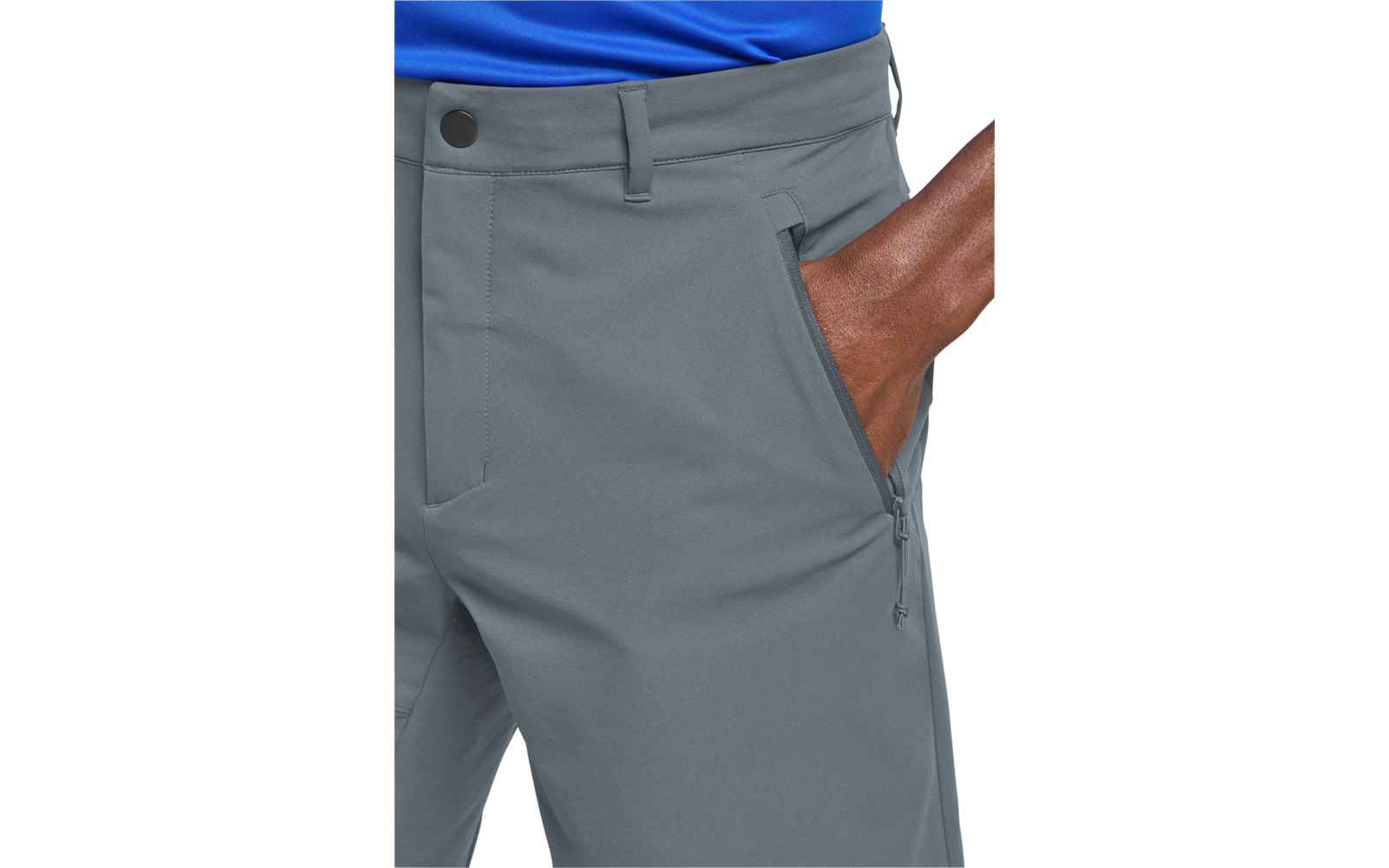 Onderlichaam van een persoon met een blauw bovenstuk en grijze broek, rechterhand in een ritssluiting-zijzak