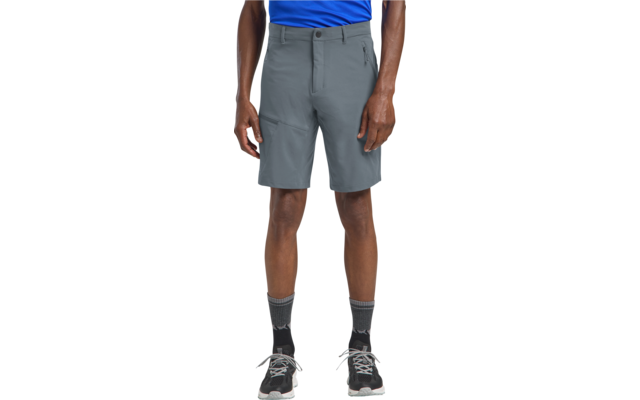 Onderlichaam van een persoon vanaf de taille, blauw bovenstuk, grijze knielange korte broek, zwarte sokken, zwarte sportschoenen, handen langs het lichaam zichtbaar