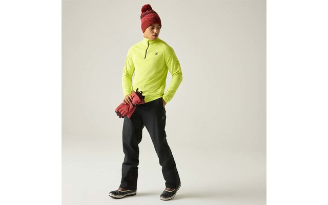 Persona con prenda superior verde neón con media cremallera, pantalones negros, gorro rojo de punto, guantes rojos en la mano, de pie sobre fondo claro