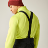 Persona vista de espaldas y de perfil, chaqueta amarillo neón, tirantes negros, gorro rojo de punto, fondo claro