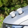 Zwei weiße Tassen auf schwarzen Untersetzern auf der Motorhaube eines silbernen Autos, unscharfer grüner Hintergrund