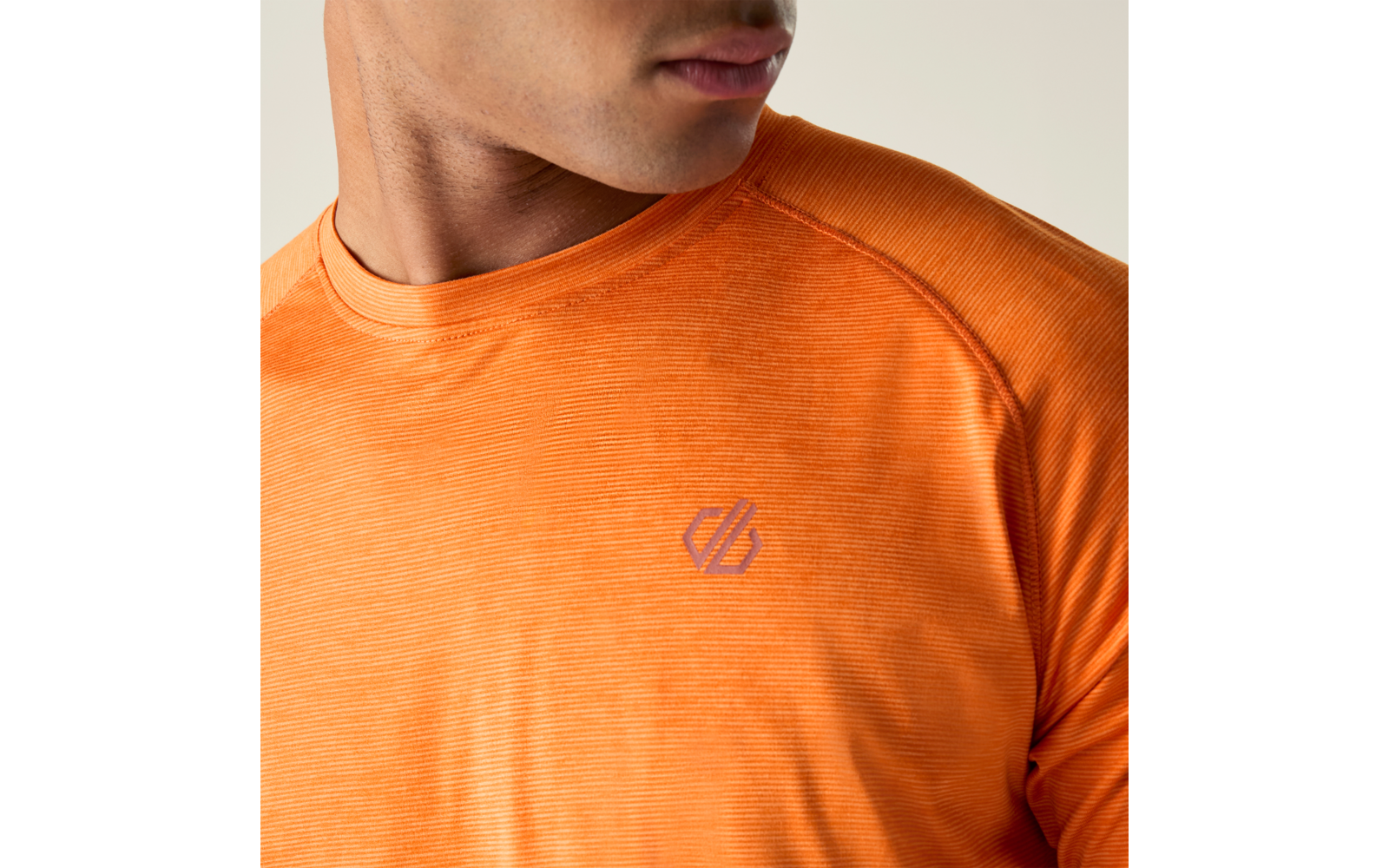 Vue partielle d'une personne du cou à la poitrine, portant un T-shirt orange à fines rayures avec un petit logo violet-gris sur la poitrine gauche