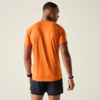 Personne de dos portant un t‑shirt orange à manches courtes et un short de sport noir, cheveux courts, bracelets noirs aux deux poignets, debout devant un fond clair uni, regarde vers la droite