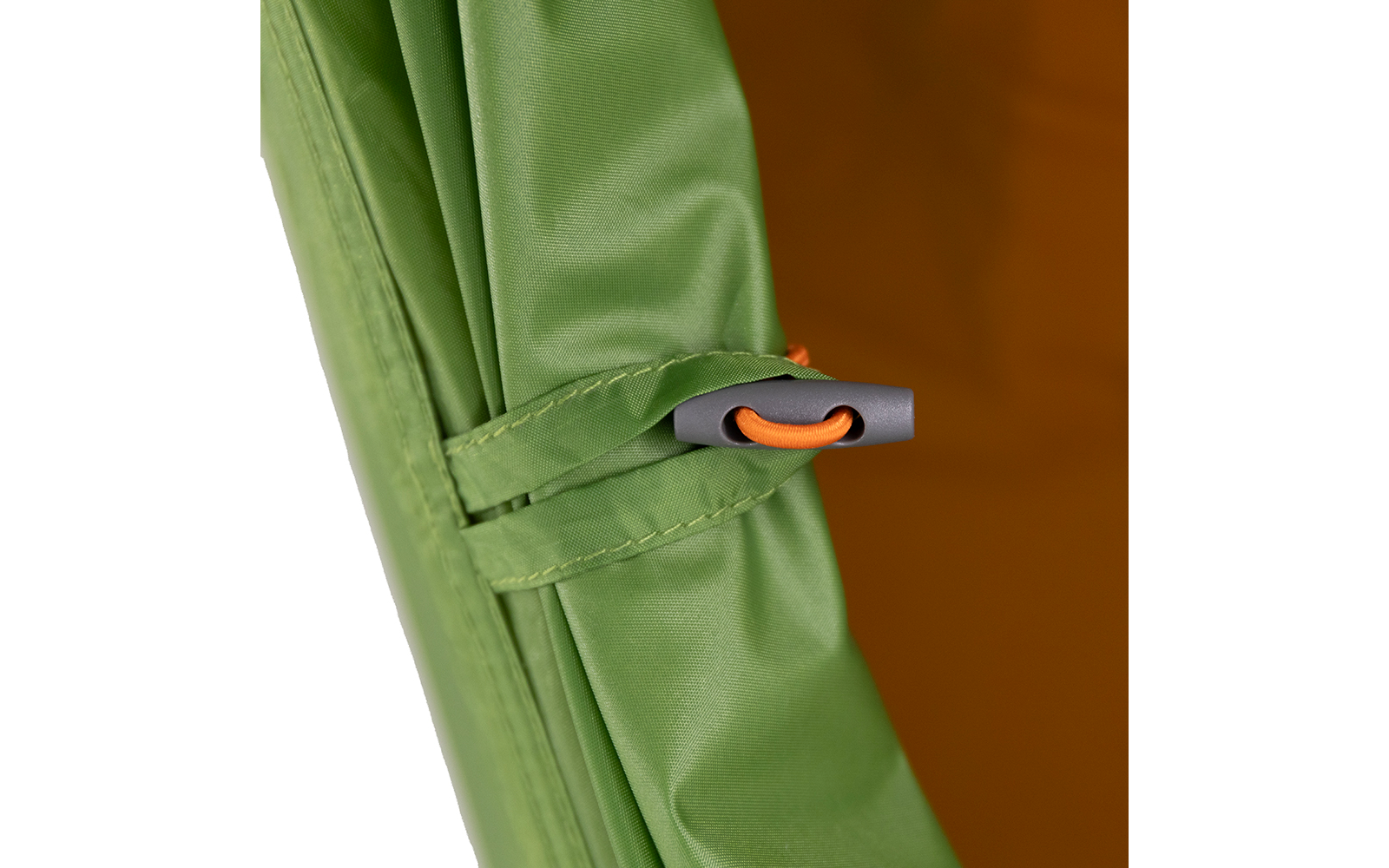 Grüne Stoffkante mit angenähter Schlaufe, grauer Kordelstopper und orangefarbene Elastikschnur; im Hintergrund braun-orangefarbener Stoff