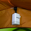 Weißes rechteckiges Camping-Licht mit Vango-Logo, an einem schwarzen Gurt unter dem orangen Zeltdach hängend; unten grüner Zeltboden sichtbar
