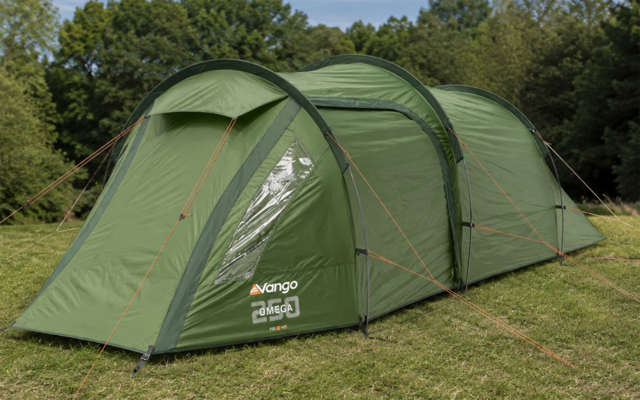 Green tunnel tent on a grassy field with guy lines and trees in the background