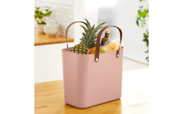 Rosafarbene Tasche mit Ananas und Obst auf einem Holztisch