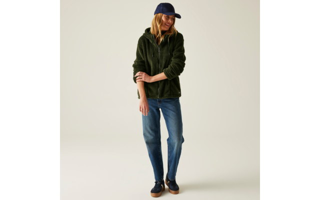 Frau mit blauer Kappe, grünem Pullover und blauen Jeans vor hellem Hintergrund