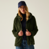 Frau mit blonden Haaren, die eine grüne Jacke und eine blaue Mütze trägt