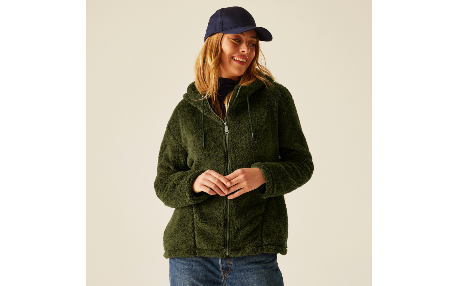 Frau trägt grüne Fleecejacke und blaue Jeans, sie trägt eine dunkelblaue Kappe
