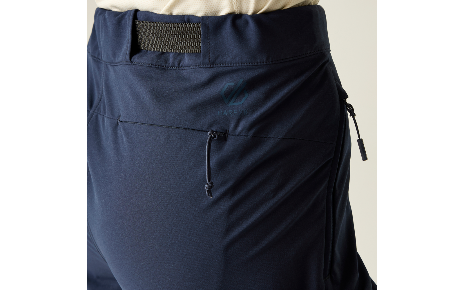 Close-up van het heupgedeelte in een donkerblauwe broek met elastische taille, zijritszak, koord en een lichtgekleurde bovenkant zichtbaar bovenaan