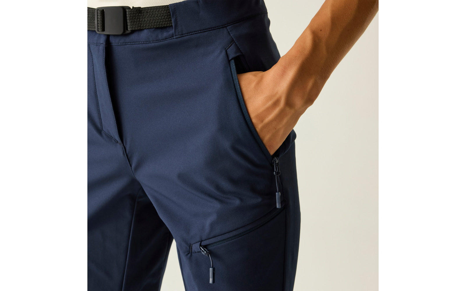 Heup- en bovenbeengebied van een persoon in donkerblauwe broek, hand in een voorvak met rits, zwarte riem zichtbaar